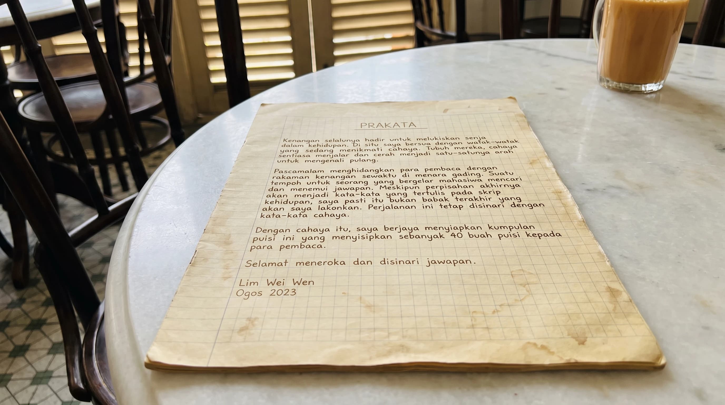 Prakata Pascamalam ditulis tangan pada helaian buku latihan lama, terletak di atas meja marmar kopitiam dengan segelas teh tarik, dinamai Lim Wei Wen, Ogos 2023. Teks penuh disediakan selepas imej.